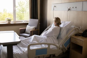 Couloir d'hôpital public avec des patients et soignants en mouvement, pris en plongée depuis l'entrée