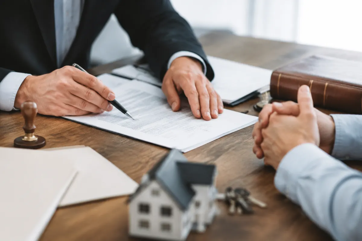 Main tenant un stylo pour signer un acte de notoriété posé sur un bureau en bois