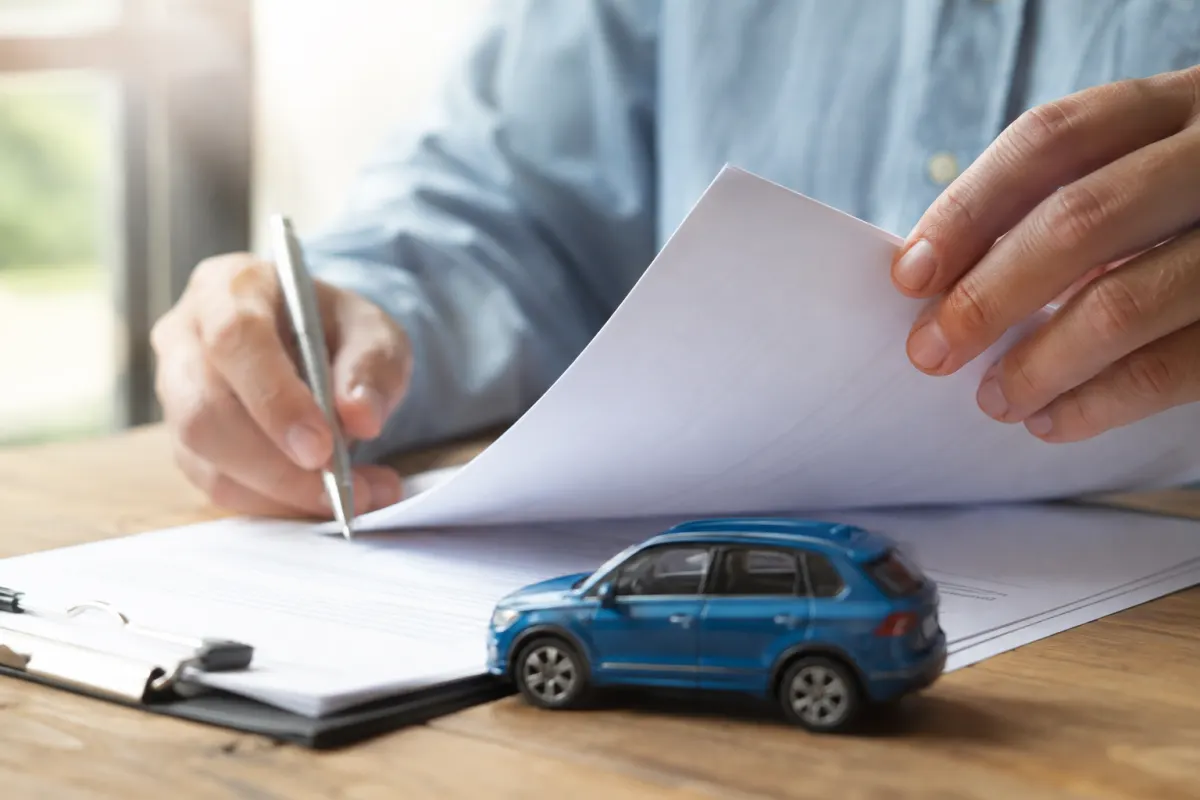 Quel est le vrai délai de rétractation pour une assurance auto ? Gros plan sur une main signant un document d'assurance automobile avec un stylo à bille bleu.